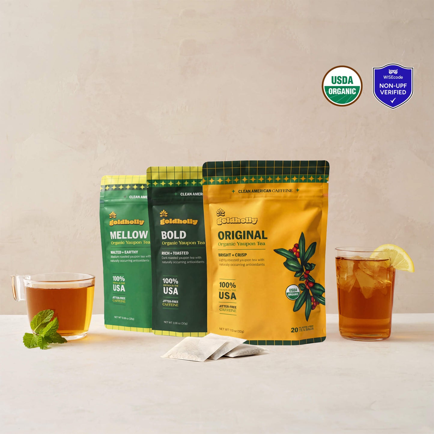Goldholly variety bundle with Original, Bold, and Mellow organic yaupon tea pouches flanked by a warm cup of brewed tea and an iced glass with lemon, with three teabags. USDA Organic certified and WISEcode Non-UPF verified.