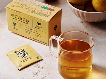 Goldholly Light Roast Yaupon tea box and individual teabag beside a glass mug of brewed golden tea