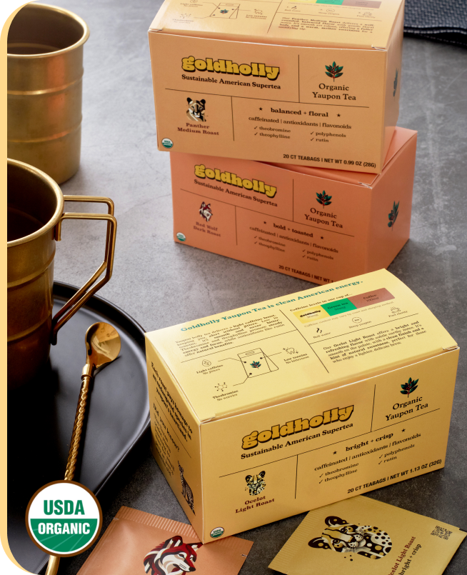 Goldholly organic yaupon tea cartons of teabags on a countertop with tea mugs and USDA organic seal