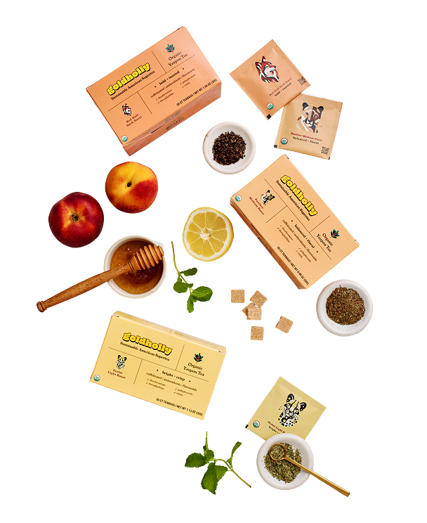 Goldholly organic yaupon tea variety flatlay featuring multiple roast cartons and teabags with fresh peaches, lemon, mint, honey, sugar cubes, and loose leaf tea